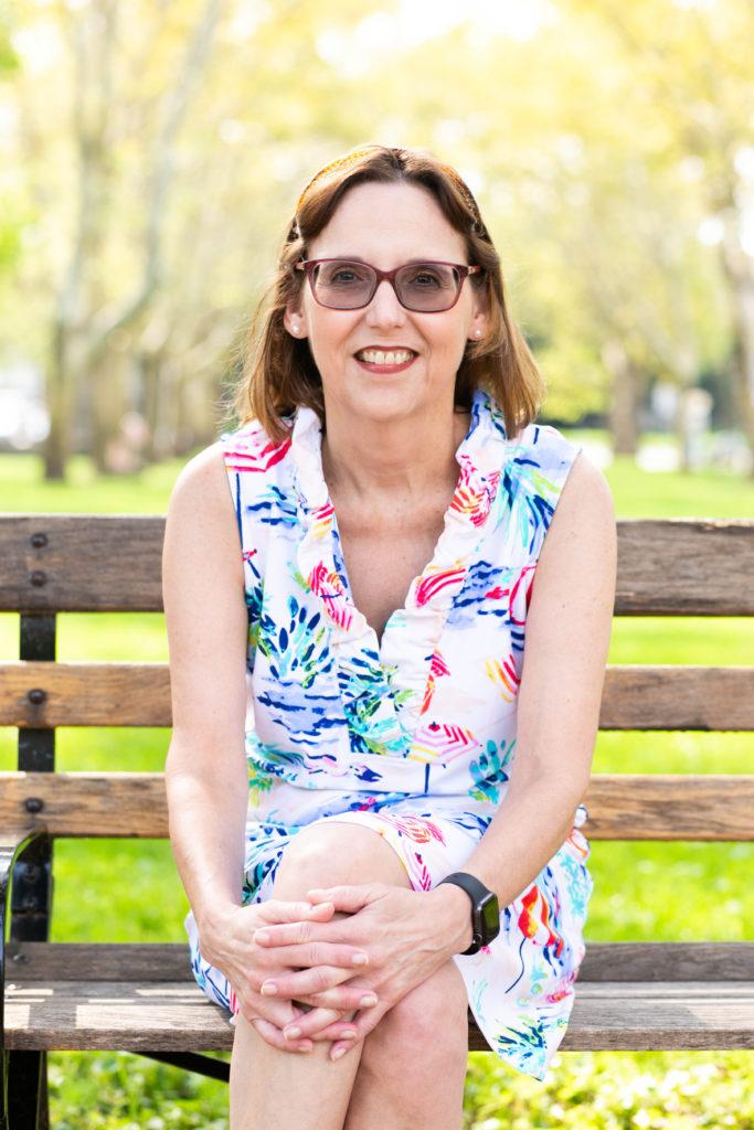 Chris Crytzer in a colorful blouse, sitting on a park bench on a sunny day